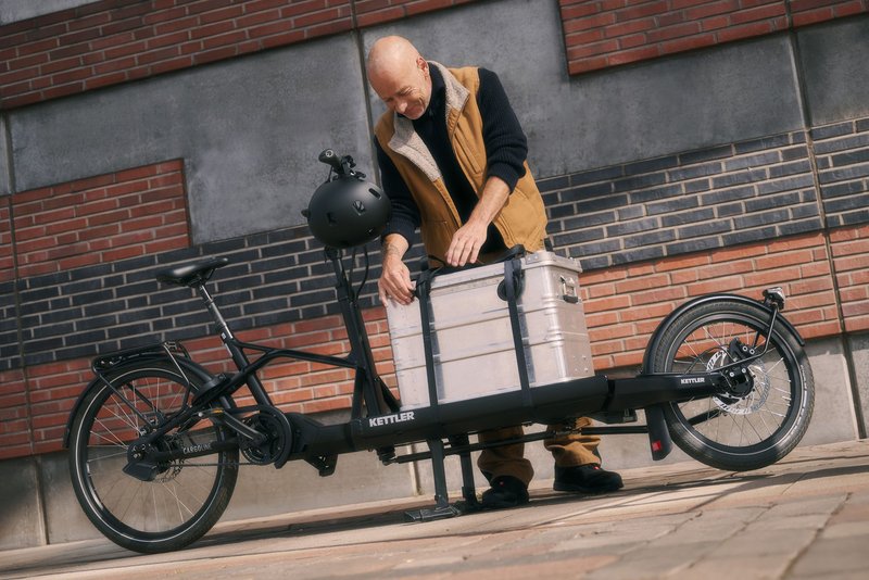 Mann befestigt Metallbox auf Lastenrad