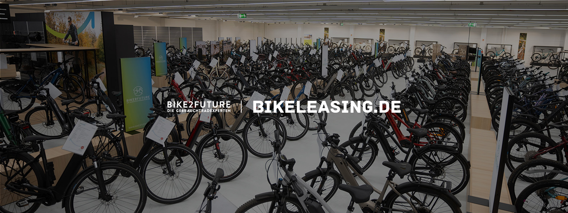 Große Ausstellungsfläche mit zahlreichen Fahrrädern und E-Bikes in einem Bike2Future-Showroom. Im Bild sind die Logos von Bike2Future und Bikeleasing.de zu sehen.