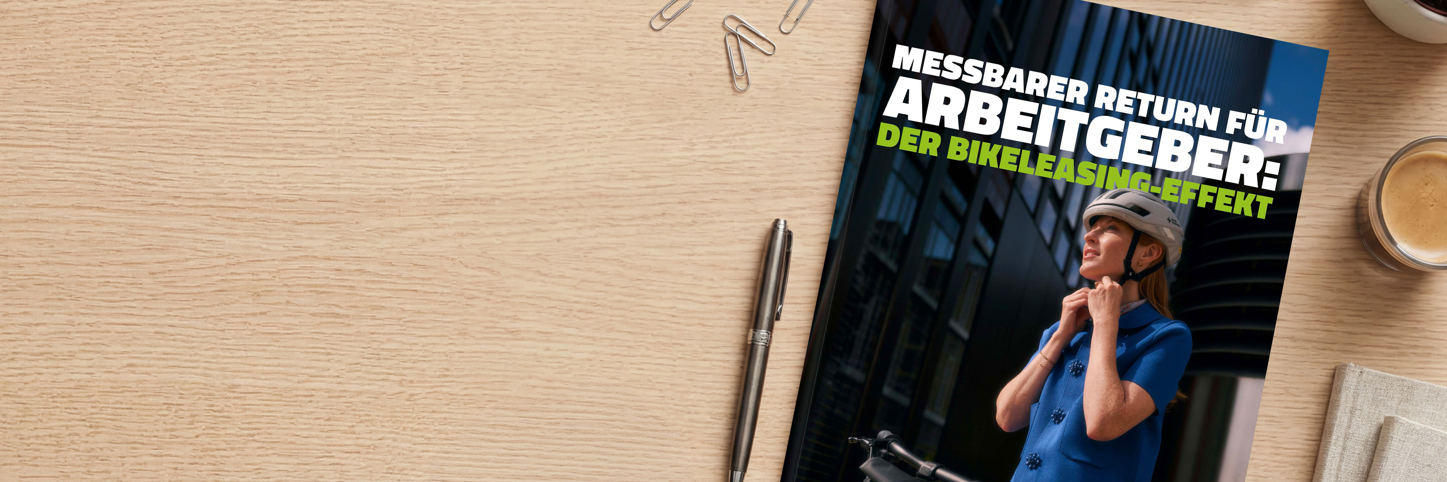 Auf einem Schreibtisch liegt ein Whitepaper mit dem Titel ‚Messbarer Return für Arbeitgeber: Der Bikeleasing-Effekt‘. Daneben befinden sich ein Stift, Büroklammern und eine Tasse Kaffee.