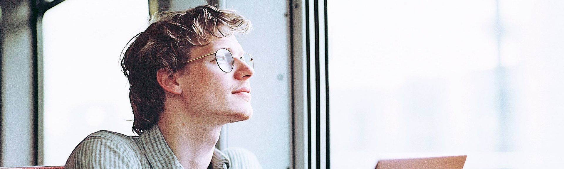 Noch flexibler unterwegs mit Mobilitätsbudget Mann sitzt mit einem Laptop in der Bahn und schaut aus dem Fenster