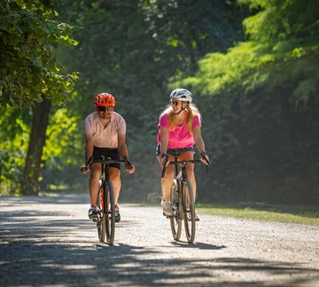 Radfahrer und Radfahrerin auf sonniger Allee