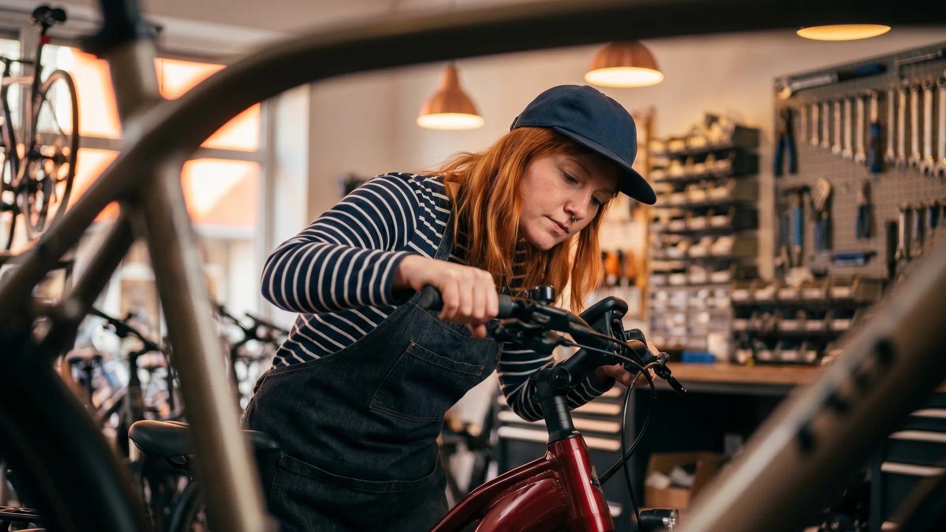  Mechanikerin in einer Fahrradwerkstatt stellt den Lenker eines E-Bikes ein; im Hintergrund hängen Werkzeuge und Ersatzteile.