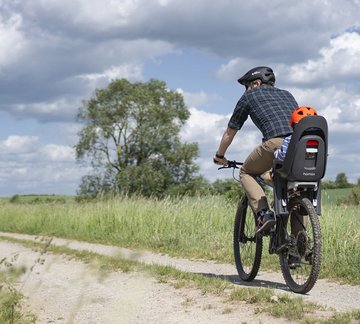 Radfahrer und Kind im Kindersitz auf Feldweg