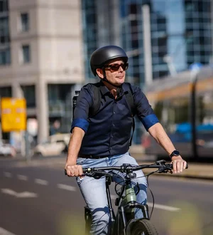 Ein Mann mit Fahrradhelm fährt mit einem Fahrrad durch eine Stadtstraße. Im Hintergrund ist eine Straßenbahn zu sehen.