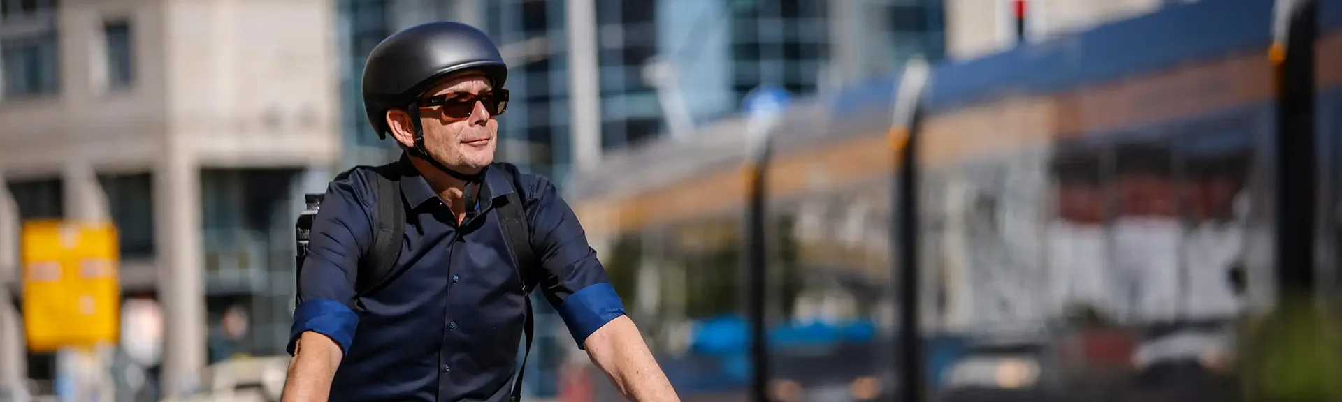 Ein Mann mit Fahrradhelm fährt mit einem Fahrrad durch eine Stadtstraße. Im Hintergrund ist eine Straßenbahn zu sehen.