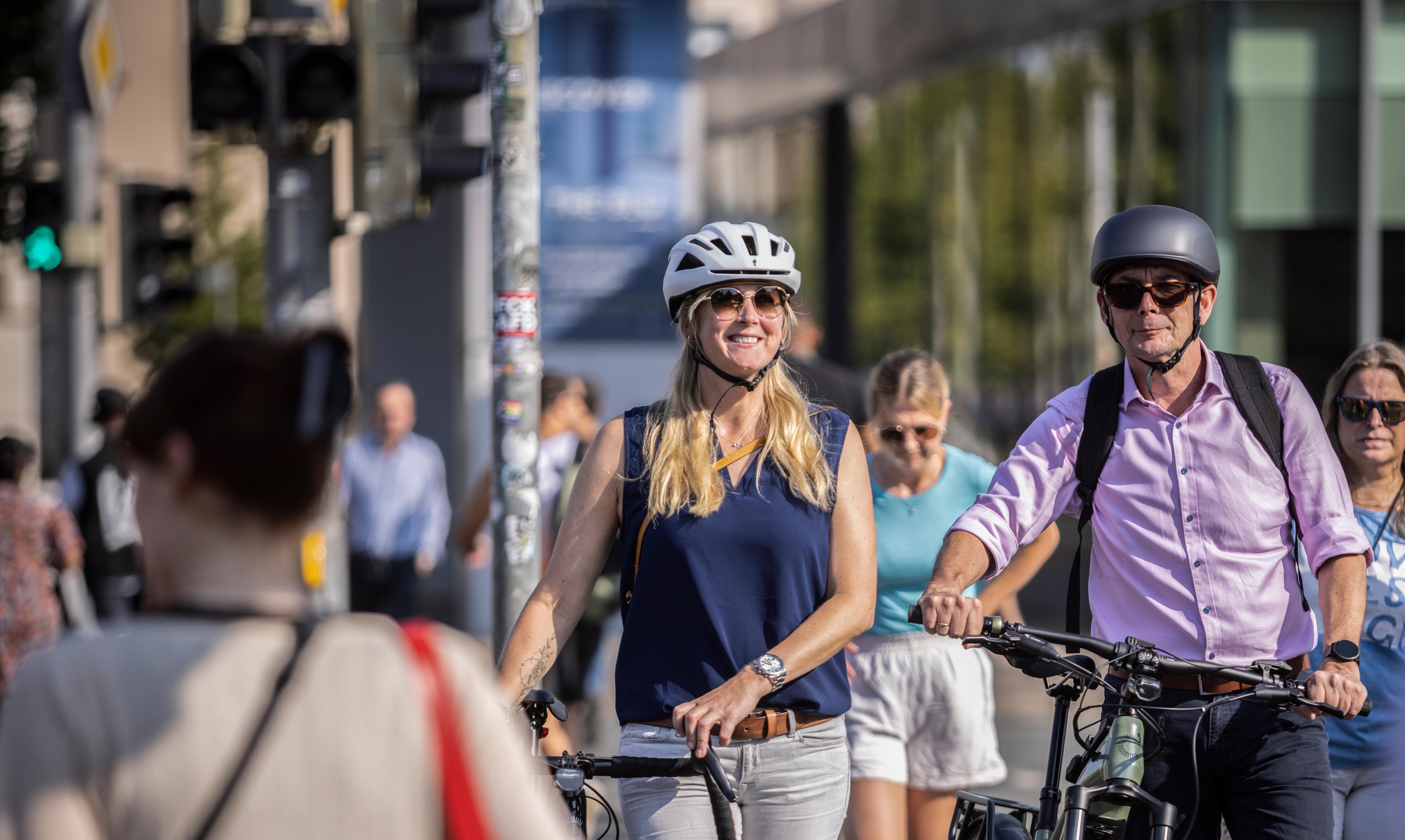 Dienstrad-Leasing und die Gesellschaft Frau und Mann mit Helm schieben Räder durch die Stadt