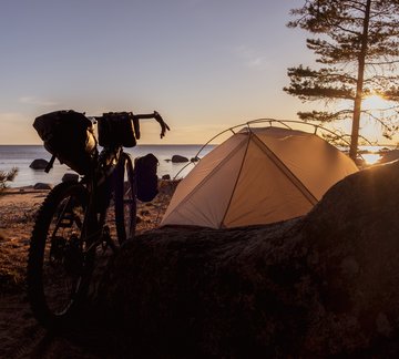 Gravelbike und Zelt am Strand bei Sonnenuntergang