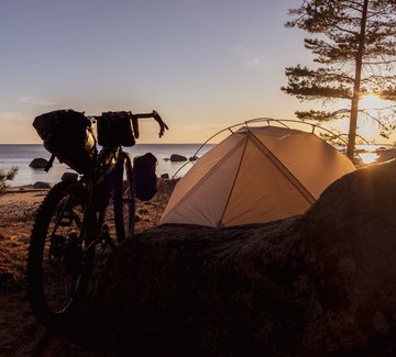 Gravelbike und Zelt am Strand bei Sonnenuntergang