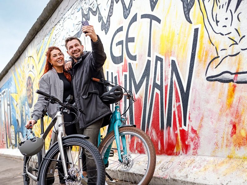 Frau und Mann mit Diensträdern vor der Berliner Mauer