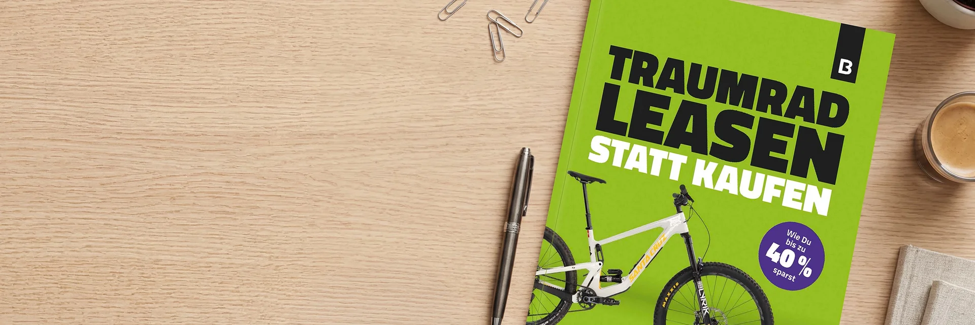 Grünes Bikeleasing-Whitepaper mit der Aufschrift ‚Traumrad leasen statt kaufen‘ auf einem Schreibtisch neben einem Stift, Büroklammern und einer Kaffeetasse.