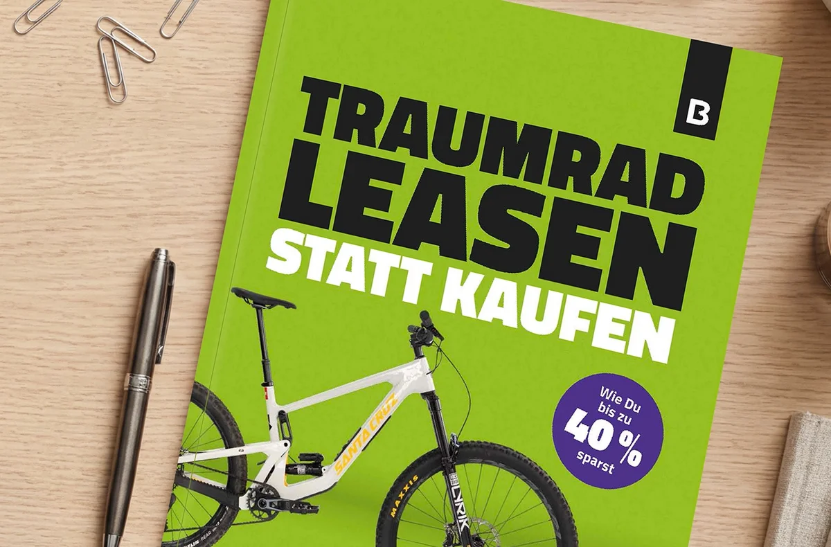 Grünes Bikeleasing-Whitepaper mit der Aufschrift ‚Traumrad leasen statt kaufen‘ auf einem Schreibtisch neben einem Stift, Büroklammern und einer Kaffeetasse.