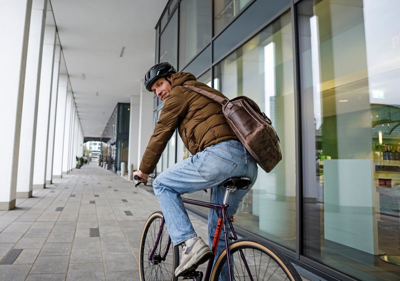 Mann mit Arbeitstasche auf Fitnessbike 